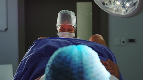 Front view of Caucasian female surgeon examining pregnant woman during delivery in operating room at