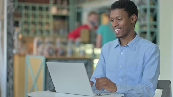 Cheerful African Businessman Doing Video Call on Laptop in Cafe 