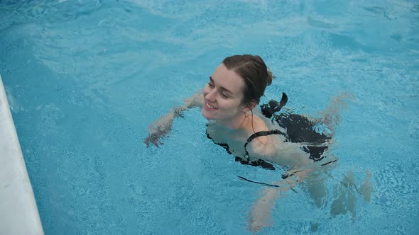 Cute Girl in a Black Swimsuit Swims in the Pool