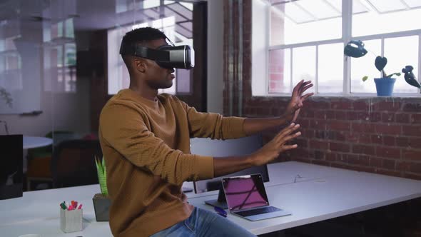 African american businessman sitting on desk using vr headset and gesturing