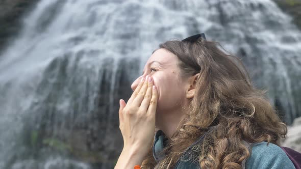 An Active Female Tourist Smears Her Face with Sunscreen Against the Background of a Large Waterfall