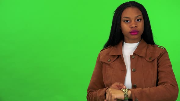 A Young Black Woman Looks at the Camera and Taps the Watch on Her Wrist - Green Screen Studio