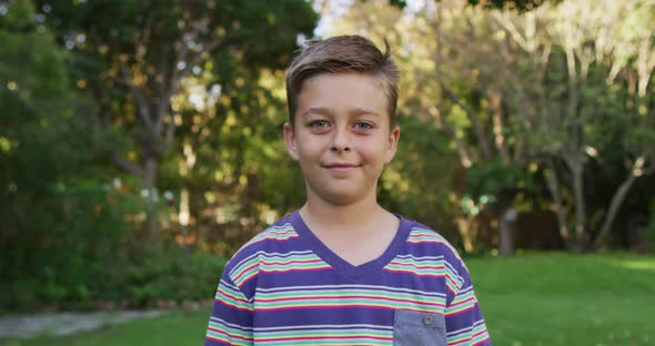 Portrait of happy caucasian boy standing in garden smiling to camera