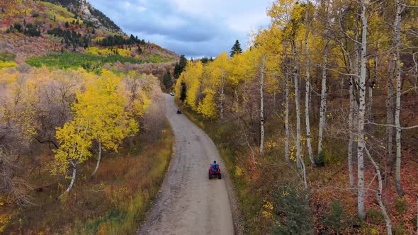 Friends riding off-road vehicles along a colorful mountain road in autumn - aerial follow view