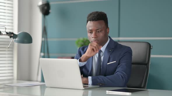 African Businessman Thinking While Working on Laptop in Office