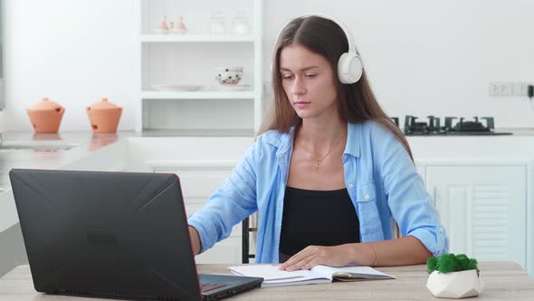 Focused Student Girl with Headphones Writing Notes at Laptop Checking Handwriting Summary Watching