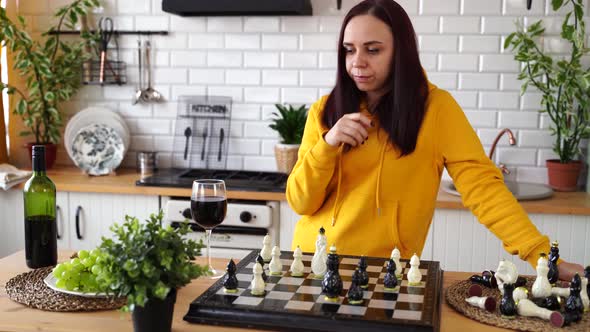 Thoughtful Young Woman Plays Chess Drinks Red Wine and Invents Move