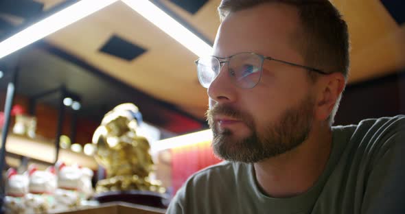 Portrait of a Pleased Bearded Man with Glasses Who is Eating Chinese Food Using Chopsticks Against