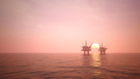 Two offshore platforms in the open sea with a pink evening sky and setting sun.