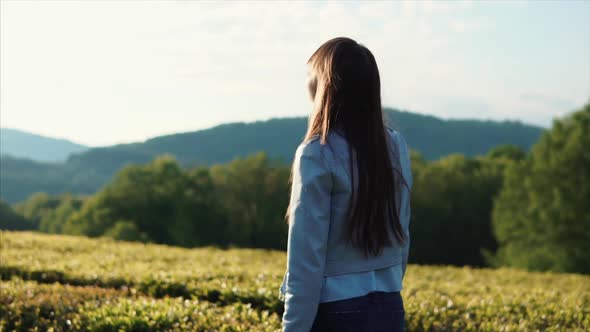 Brunette Girl Is Walking Calmly Between Green Bushes in a Garden Near Mountains