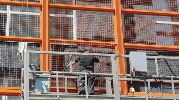 A Builder on a Lift Installs a Protective Metal Mesh on the Facade of the House