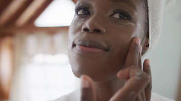 Portrait of african american attractive woman applying face cream in bathroom