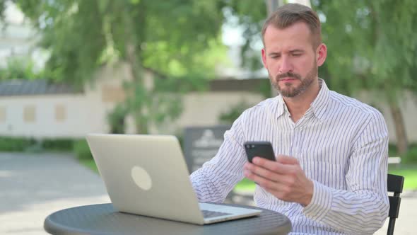 Attractive Middle Aged Man Browsing Internet on Smartphone in Outdoor Cafe