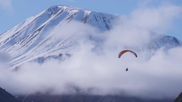 Paraglider flies next to mountain peaks
