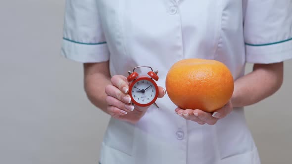Nutritionist Doctor Healthy Lifestyle Concept - Holding Organic Grapefruit Fruit and Alarm Clock