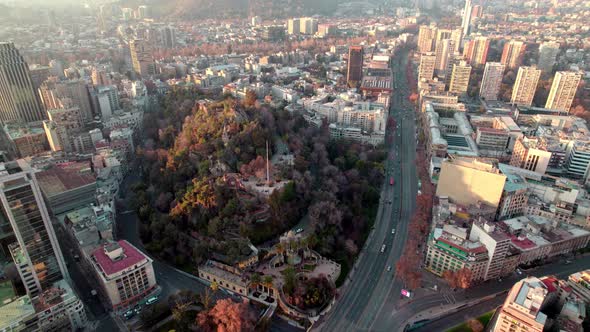 Aerial view dolly over Santa Lucia hill covered with autumnal trees, traffic in highway and Santiago