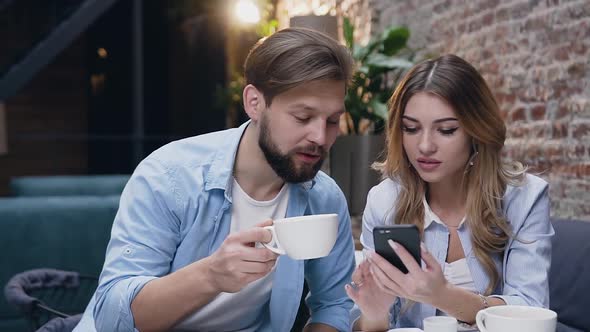 Guy and Blond Woman with  which Sitting Together in Hotel and Drinking Tea During Using Phone