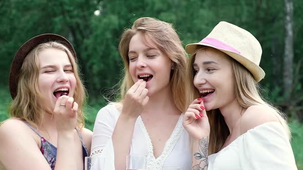 young girls in hats in forest on picnic on summer day eat red ripe cherry berry