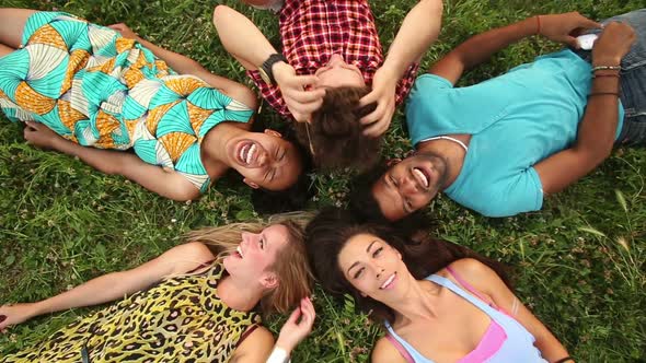 Group of happy friends forming a circle with their heads laying back on grass