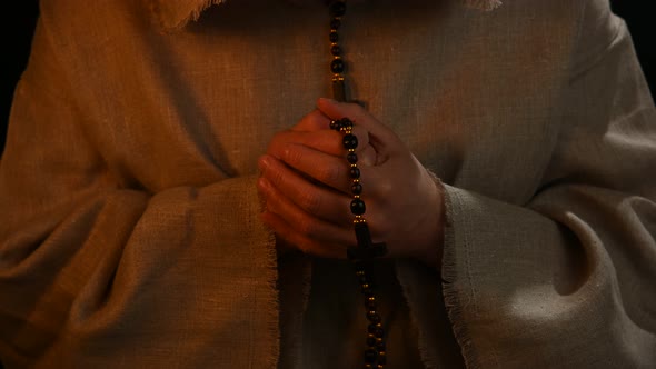 Monk in haircloth cowl robe praying in candlelight