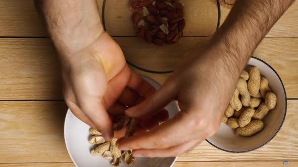 View from above male hands peeling roasted peanuts from their shells. Close-up. Wooden background