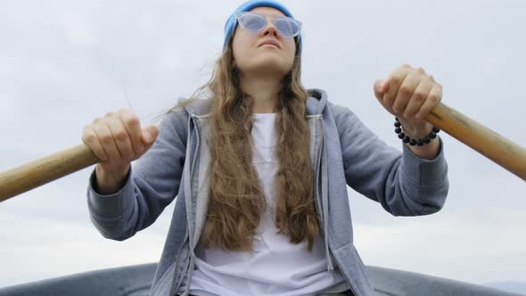 A Girl with Flowing Hair in a Blue Cap and Sunglasses Floats on a Rowing Boat