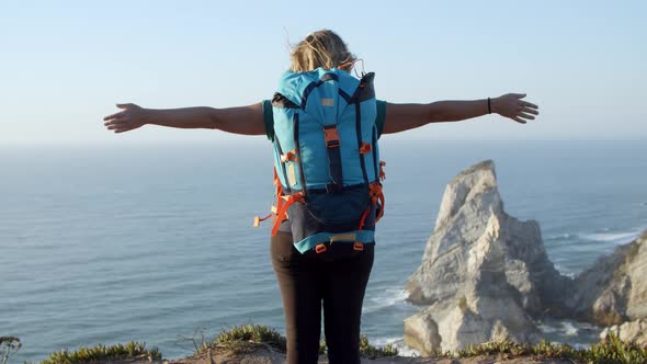 Excited Female Backpacker Standing at Rocky Cliff