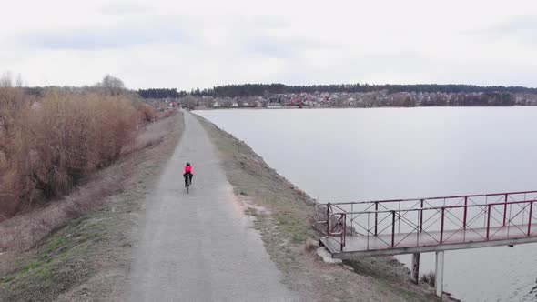 Cyclist is pedalling on road bike along dam on gravel road. Cycling concept