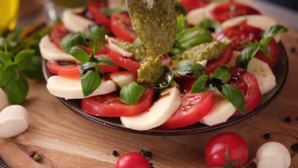 Pouring Pesto Sauce on Caprese Salad with Cherry Tomatoes and Mozzarella Cheese Balls