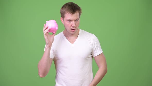 Young Handsome Man Shaking Piggy Bank