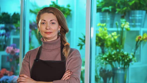 Woman Florist is Looking at the Camera, on the Background of a Showcase of Flowers.