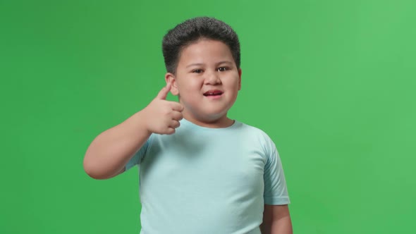 Happy Asian Little Boy Showing Thumbs Up Gesture While Standing In The Green Screen Studio