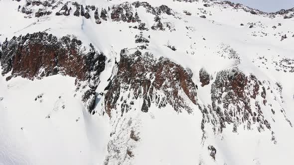 Deep Trench Between Cliffs on Snowy Slope of Large Mountain