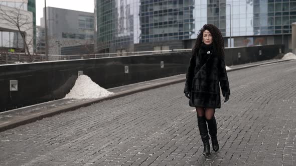 A Curlyhaired Stylish Middleaged Brunette Woman in a Black Fur Coat Walks Alone in the City on a