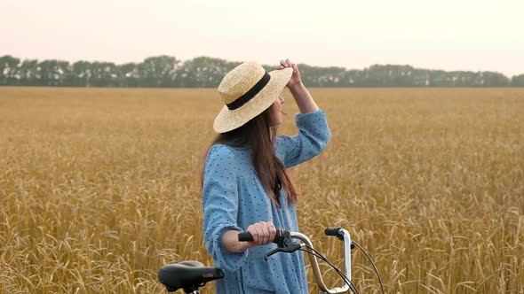 woman walks rural road along wheat field on bike on summer sunset