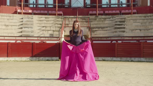 Young Female Bullfighter With Muleta Standing In Middle Of Bullring With Empty Tiered Rows