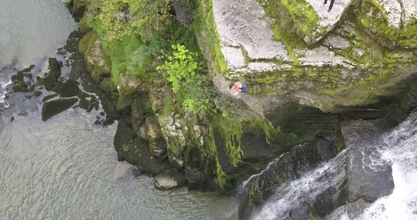 Young Cliff jumping athlete dives from a rock next to a waterfall in the Doubs river, Neuchatel, Swi