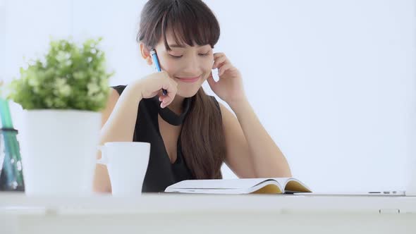 Young asian woman smiling sitting in the living room study and learning writing notebook at home.