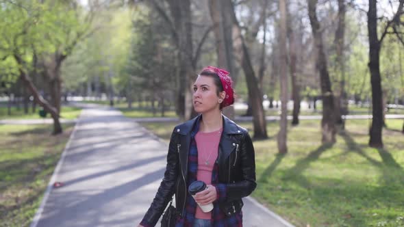 Beautiful Young Stylish Woman Walks in the Park with a Cup of Coffee. Modern Girl in a Leather