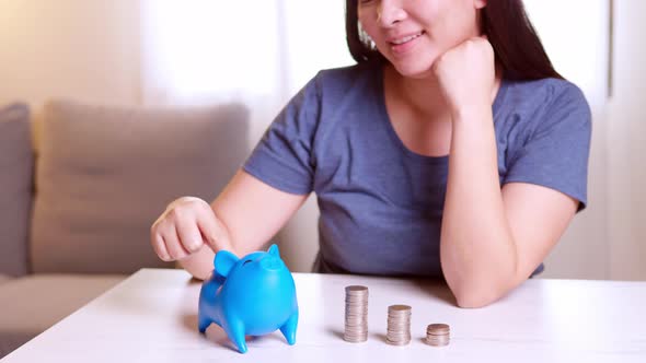 Stack of coins with a young woman putting coins into the blue piggy bank. Saving money for future in