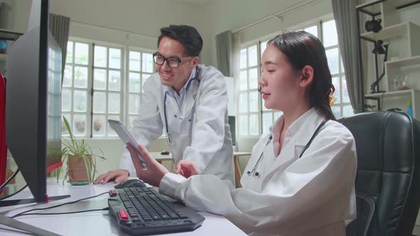 Medical Doctor's Office: Two Asian Professional Physicians Talking, Consulting And Working On Tablet