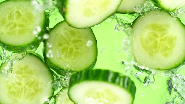 Super Slow Motion Shot of Cucumber Slices Falling Into Water on Green Background at 1000Fps.