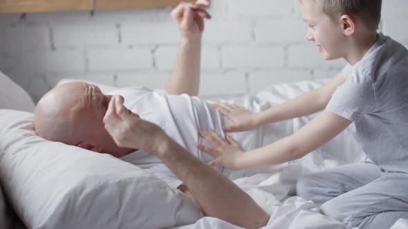 Playful Schoolboy Laughing and Trying to Wake Up his Father