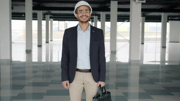 Slow Motion Portrait of Cheerful Middle Eastern Man in Suit and Safety Helmet Standing in Empty
