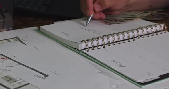 Man Counts the Money and Writes the Result to the Note with Dollar Bills on the Table Accountant