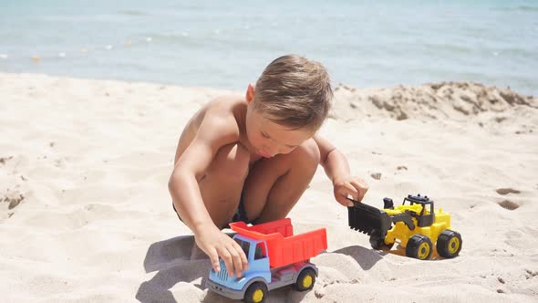 Cute Child, Boy Playing with Cars on a Sandy Beach, Plastic Toy Car, Excavator. A Child and the