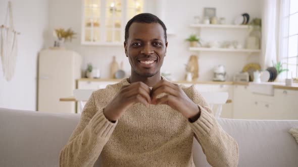 Happy Man Shows Love Making Heart Shape Gesture on Sofa