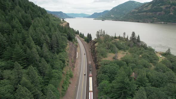 Aerial dolly forward following freight train, highway traffic along Columbia River.