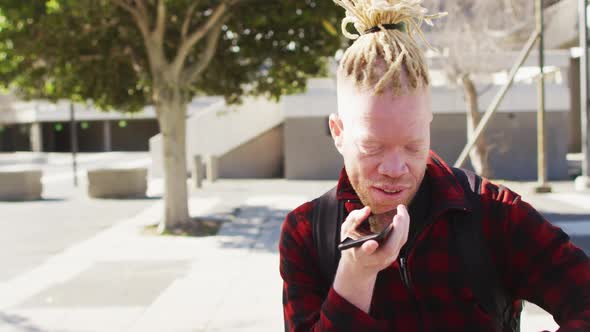Happy albino african american man with dreadlocks in park talking on smartphone