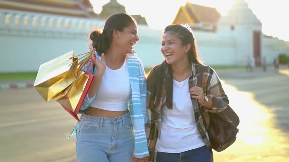Two happy Asian women shopping outdoor in good mood walking on street with shopping bags and talking